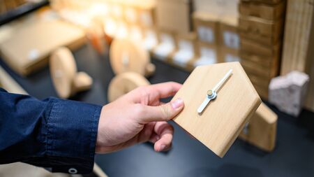 Male hand customer choosing wooden clock in art and craft decor shop. Buying instrument of time for home decoration. Time conceptの写真素材