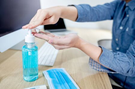 Washing hands by alcohol sanitizer or alcohol gel from pump bottle while working from home. Coronavirus (COVID-19) pandemic infection prevention. Hygiene and health care during working at home office.の写真素材