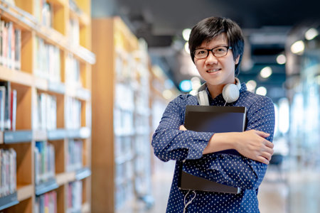 Asian man university student holding book near bookshelves in college library for education research. Bestseller collection in bookstore. Scholarship or educational opportunity conceptsの写真素材