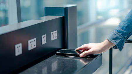 Male hand putting smartphone on wireless charger or induction charger. Mobile phone power charging service station in public area.の写真素材