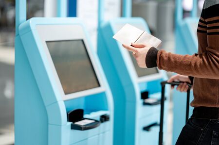 Male tourist holding passport and smartphone using self check-in kiosk in airport terminal. Travel abroad conceptの写真素材