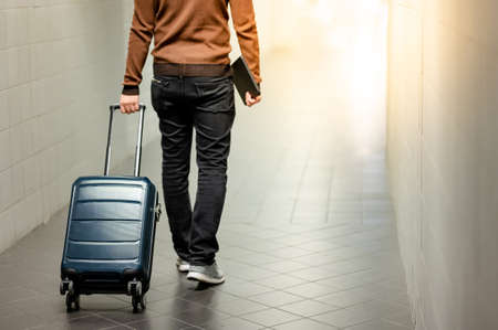 Travel insurance concept. Male tourist carrying suitcase luggage and digital tablet walking in airport terminal.の写真素材