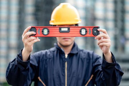 Asian maintenance worker man holding red aluminium spirit level tool or bubble levels at construction site. Equipment for civil engineering projectの写真素材