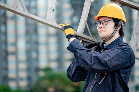 Asian maintenance worker man with protective suit and safety helmet carrying aluminium step ladder...