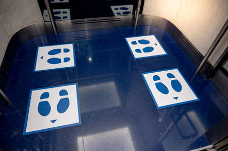 Blue glossy floor of passenger lift or elevator with standing marker for social distancing to avoid spreading coronavirus. Foot symbol position for preventing COVID-19 pandemic in public building.の写真素材