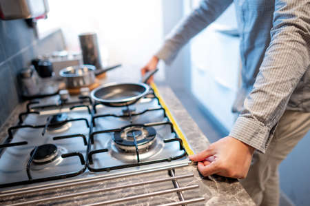 Male hand interior designer using tape measure on gas stove on modern countertop in kitchen showroom. Shopping appliance for domestic kitchen. Home improvement conceptの写真素材