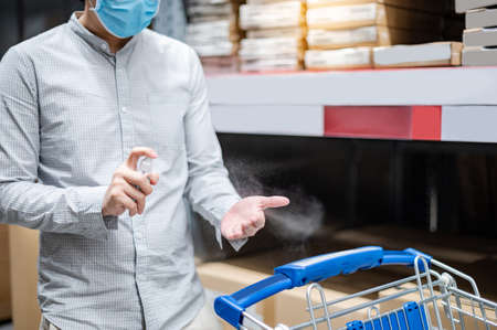 Cleaning hand with sanitizer spray. Asian man spraying alcohol to prevent Coronavirus (COVID-19) infection while shopping in supermarket or grocery store. Health care with antibacterial product.の写真素材