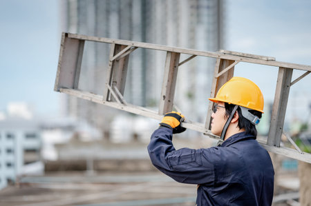 Asian maintenance worker man with protective suit and safety helmet carrying aluminium step ladder...