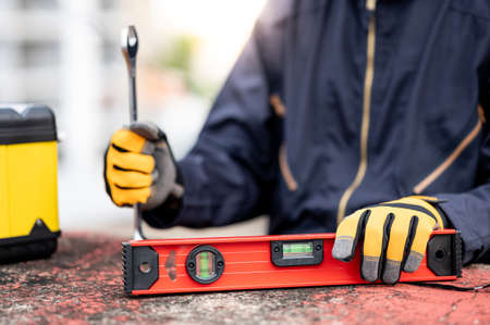 Male mechanic hand or maintenance worker man wearing protective suit holding wrench and aluminium spirit level tool or bubble levels at construction site. Equipment for mechanical engineering projectの写真素材