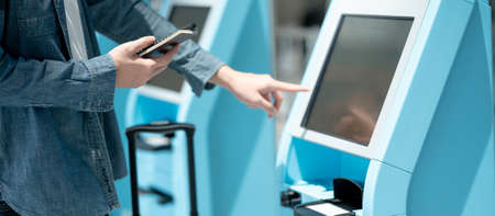 Male tourist holding passport and smartphone using self check-in kiosk in airport terminal. Travel abroad conceptの写真素材