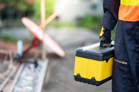Male maintenance worker hand carrying yellow work tool box at construction site. Equipment for...
