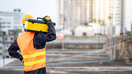 Asian maintenance worker man wearing protective suit and safety helmet carrying work tool box at construction site. Equipment for civil engineering projectの写真素材