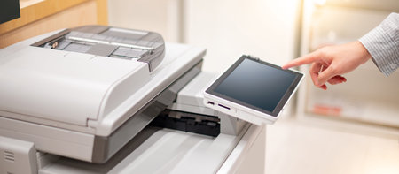 Male hand touching button on control panel of photocopier copying and printing report paperwork in...