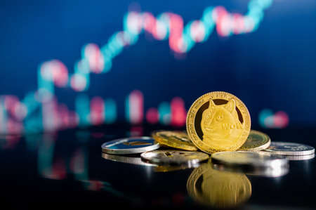 Gold Dogecoin and other crypto coins on reflecting table. Blurred candlestick chart in the background. DOGE is the most popular meme coin in cryptocurrency world.の写真素材