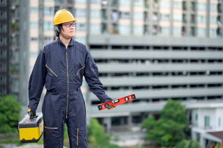 Asian maintenance worker man wearing protective suit and helmet holding red aluminium spirit level...