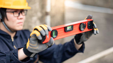 Asian maintenance worker man holding red aluminium spirit level tool or bubble levels at construction site. Equipment for civil engineering projectの写真素材