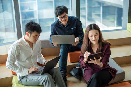 Business meeting and teamwork concept. Asian businesswoman explaining project data report to colleagues using digital tablet for presentation at workplace. Coworkers team brainstorming ideas in officeの写真素材