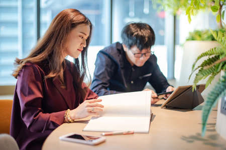 Business meeting and teamwork concept. Asian colleagues discussing about project report using note book and digital tablet at workplace. Coworkers team brainstorming ideas in green office.の写真素材