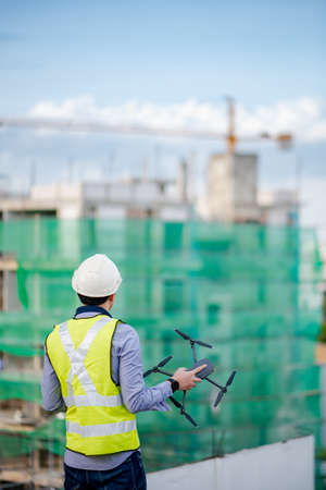 Asian engineer man holding drone at construction site. Male worker using unmanned aerial vehicle (UAV) for land and building site survey in civil engineering project.の写真素材