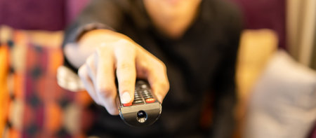 Close up of male hand using remote controller while watching TV on sofa in home theater room. Home...
