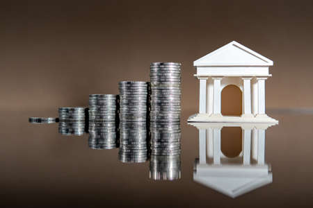 Banking concept. Bank account interest rate growth. Bank model with coins stacked on glossy table.の写真素材