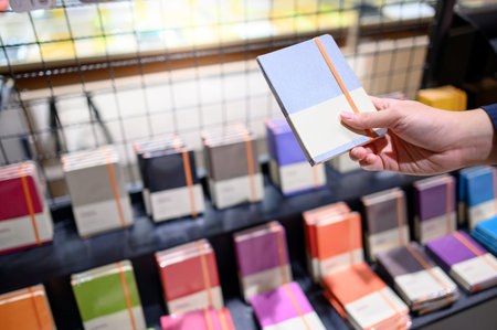 Male hand customer choosing new paper notebook from colorful display rack in stationery shop. Buying office supply conceptの写真素材