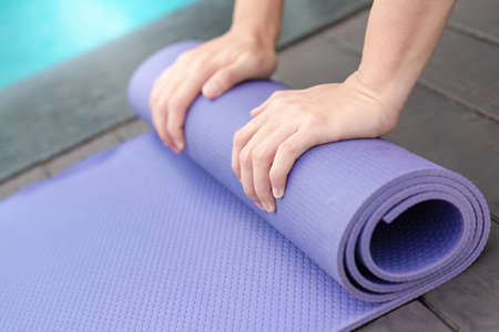 Hand rolling purple yoga mat at swimming pool. Outdoor exercise and healty lifestyle conceptの写真素材