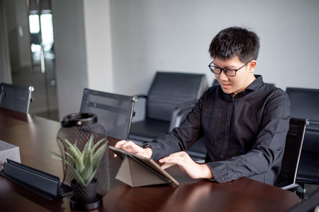 Young Asian businessman using digital tablet in office meeting room. Male entrepreneur reading news...