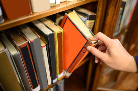 Male university student hand choosing and picking old book from old wooden bookshelf in college library. Antique textbook resources for education research. History, Law and Literature learningの写真素材