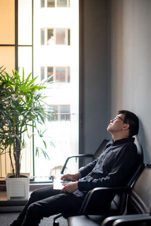Overworked Asian Businessman feeling stressed, tired and headache sitting with digital tablet in meeting room. Depression from business problem. Mental health illness or office syndrome conceptの写真素材