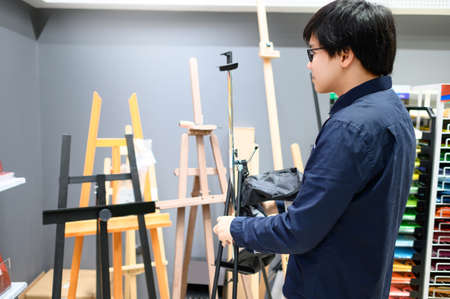 Asian man artist choosing art frame stand in stationery shop. Shopping art supplies conceptの写真素材