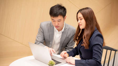 Business talk and discussion concept. Asian woman secretary and male boss manager discussing about project report using laptop computer. Well-dressed business people working in office meeting room.の写真素材