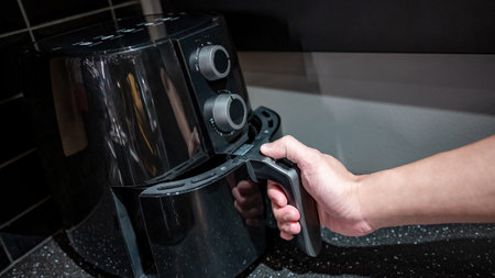 Male hand holding an electric air fryer handle in the kitchen. Home appliance for healthy cooking lifestyle.の写真素材