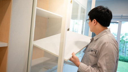 Home renovation or House remodeling concept. Asian male furniture assembler or Interior construction worker man installing white shelf panel in the cabinet. Furniture installation for the new house.の写真素材