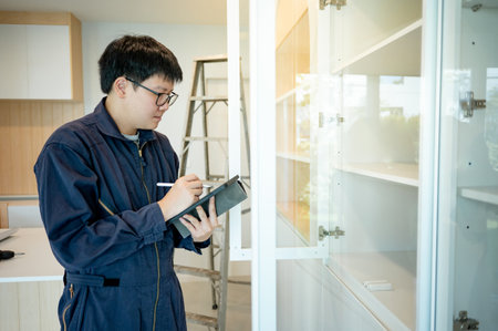 Home renovation or House remodeling concept. Asian male interior construction worker or furniture assembler man using digital tablet checking glass panel of cabinet installation.の写真素材