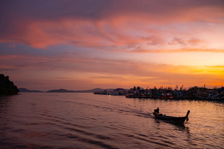 Stunning colorful sunset sky with traditional longtail boat speeding at fisherman village in phuket, Thailand.の写真素材