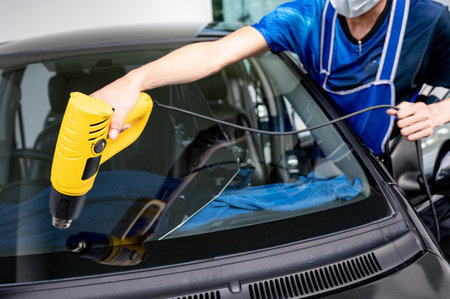 Auto specialist worker hand blowing hot air dryer or hairdryer removing old car window film tint and installing the new one. Car front windscreen film removal and tinting installationの写真素材