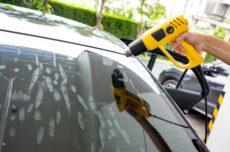Auto specialist worker hand blowing hot air dryer or hairdryer removing old car window film tint and installing the new one. Car rear windscreen film removal and tinting installationの写真素材
