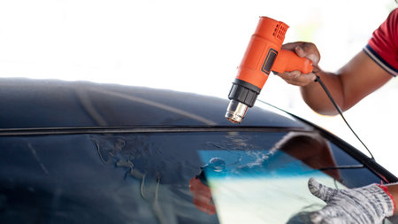 Auto specialist worker hand blowing hot air dryer or hairdryer removing old car window film tint and installing the new one. Car front windscreen film removal and tinting installationの写真素材