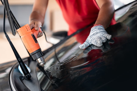Auto specialist worker hand blowing hot air dryer or hairdryer removing old car window film tint and installing the new one. Car front windscreen film removal and tinting installationの写真素材
