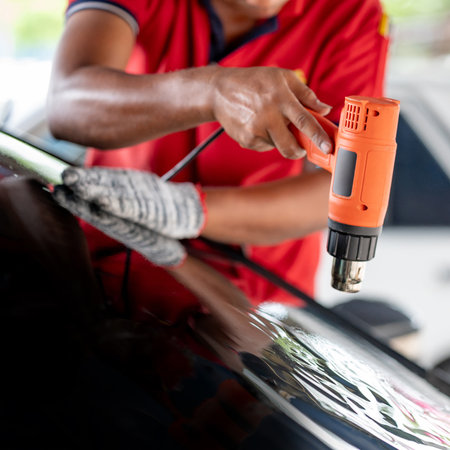 Auto specialist worker hand blowing hot air dryer or hairdryer removing old car window film tint and installing the new one. Car front windscreen film removal and tinting installationの写真素材