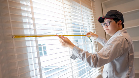 Home renovation or House remodeling concept. Asian male furniture assembler or Interior construction worker man using tape measure on metal white blinds on the window.の写真素材