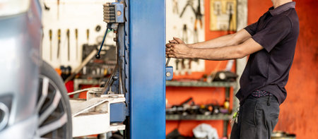 Fixing and maintenance car service in auto repair shop. Male auto mechanic lifting car on hydraulic...