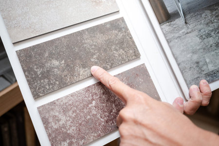 Flooring material design collection. Designer hand pointing at stone tile sample on display catalog....