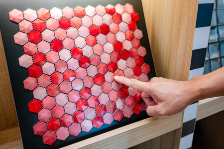 Designer hand pointing at red hexagon pattern mosaic tile on ceramic collection display shelf in...