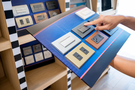 Customer hand pointing and choosing light switch and electric socket on product sample display board in home hardware store. Lighting and electrical system fixturesの写真素材