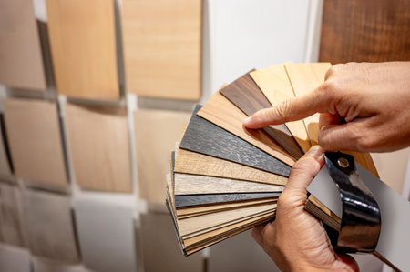 Designer hand pointing at sample of wood laminated from natural collection in material showroom. Choosing wooden veneer texture or MDF board swatch fan set for interior finishing or furniture designの写真素材