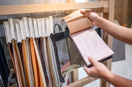 Designer hand choosing fabric pieces from fabric swatch material. Upholstery sample collection hanging on showcase rack. Textile industry for home interior design and furniture finishing decorの写真素材
