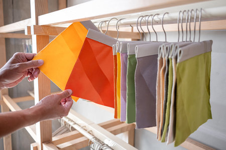 Stylist hand comparing fabric pieces from fabric swatch material. Upholstery sample collection hanging on showcase rack. Textile industry for home interior design and furniture finishing decorの写真素材