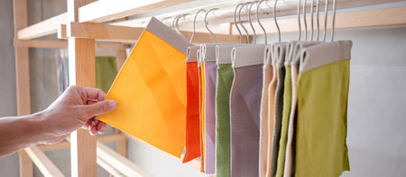 Stylist hand choosing yellow fabric piece from fabric swatch material. Upholstery sample collection hanging on showcase rack. Textile industry for home interior design and furniture finishing decorの写真素材